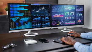 Operator analyzing Smart Manufacturing dashboards on dual monitors with real-time data visualizations for production, inventory, and quality control.